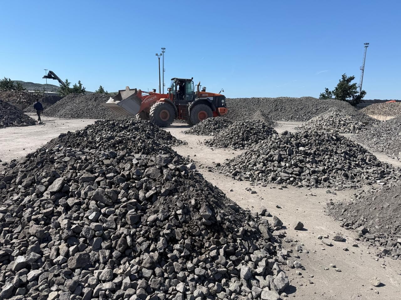 Mineral stockpiles in an open yard, with a loader